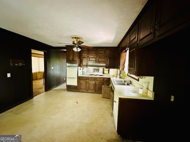 kitchen with white double oven, wooden walls, sink, dark brown cabinets, and ceiling fan