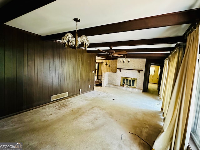 unfurnished living room featuring a fireplace, ceiling fan with notable chandelier, beam ceiling, and wooden walls