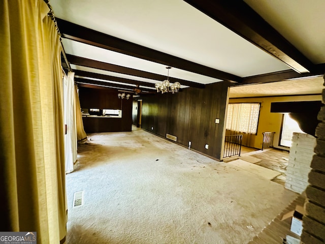 unfurnished living room featuring a fireplace, a chandelier, wood walls, beam ceiling, and light colored carpet