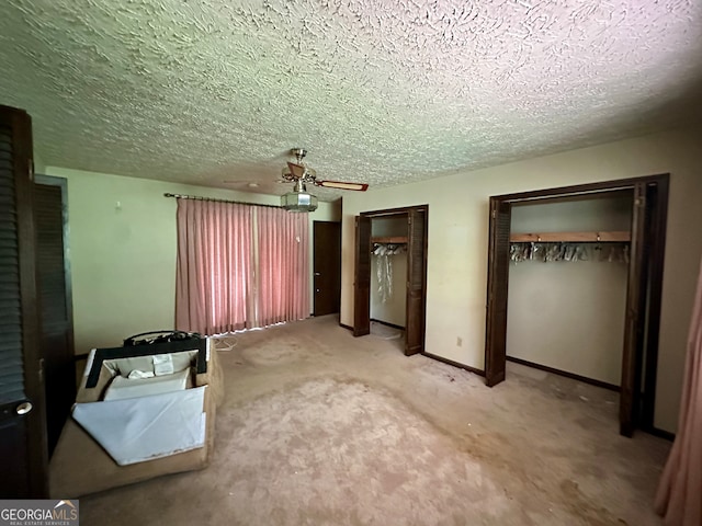 unfurnished bedroom with a textured ceiling, carpet, two closets, and ceiling fan