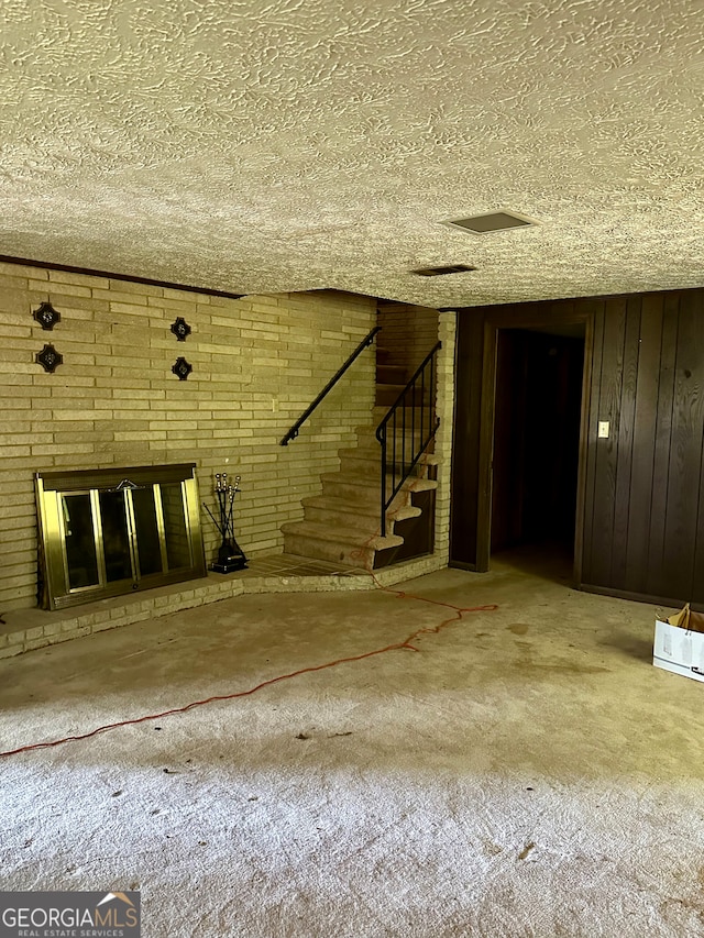 unfurnished room with a textured ceiling, a brick fireplace, wood walls, and concrete flooring