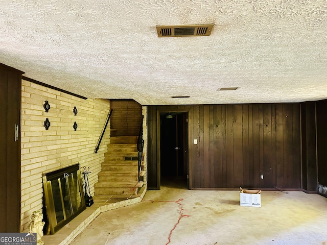 unfurnished living room featuring a textured ceiling, a brick fireplace, brick wall, and wood walls