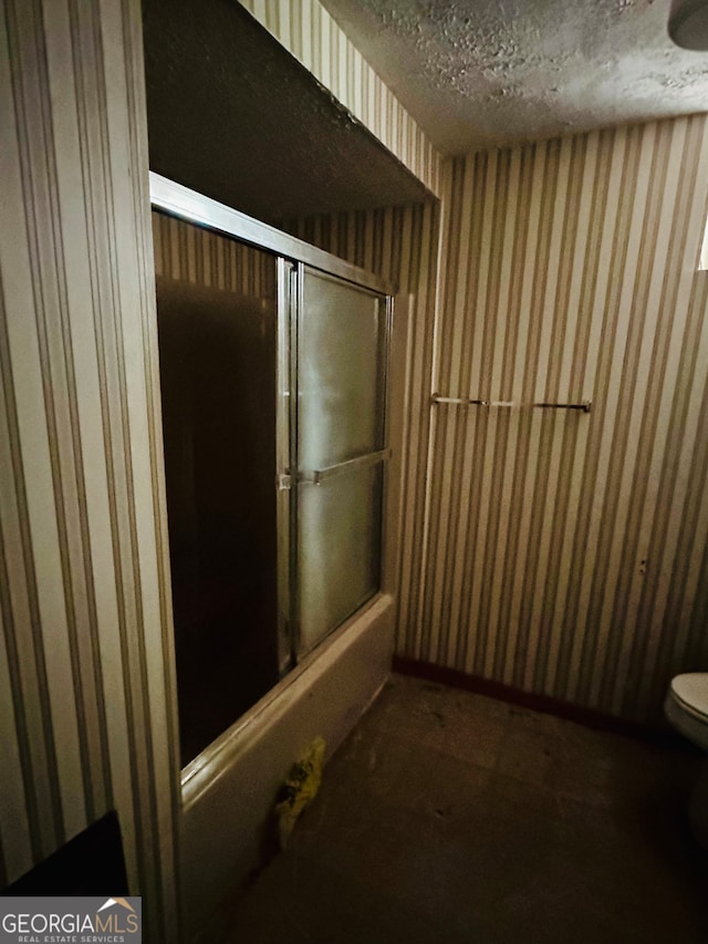 bathroom with enclosed tub / shower combo, toilet, and a textured ceiling