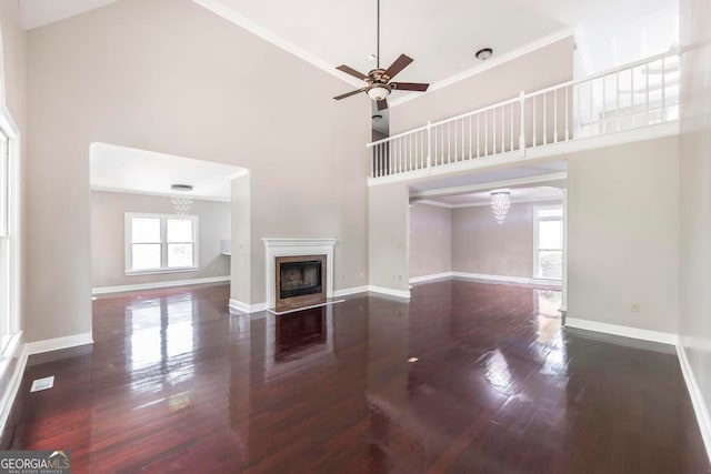 unfurnished living room featuring high vaulted ceiling, a high end fireplace, ceiling fan with notable chandelier, ornamental molding, and dark wood-type flooring