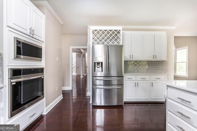 kitchen with white cabinets, backsplash, appliances with stainless steel finishes, dark hardwood / wood-style flooring, and ornamental molding