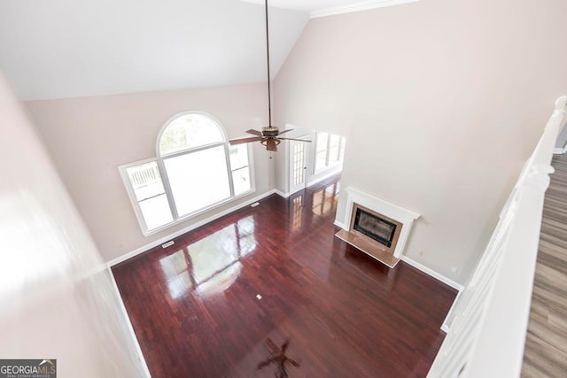 unfurnished living room featuring high vaulted ceiling, ornamental molding, a premium fireplace, ceiling fan, and dark hardwood / wood-style floors