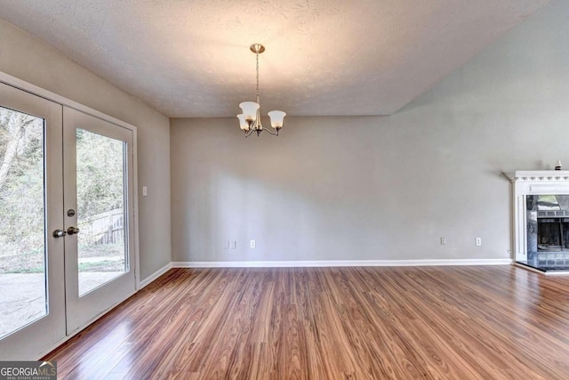 unfurnished dining area with a textured ceiling, plenty of natural light, an inviting chandelier, and hardwood / wood-style floors