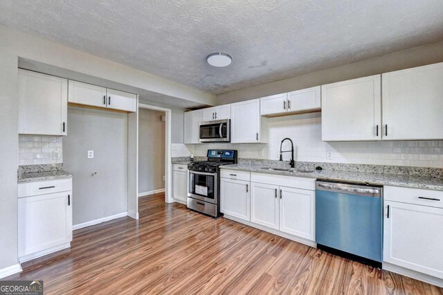 kitchen with appliances with stainless steel finishes, sink, white cabinetry, light stone counters, and light wood-type flooring