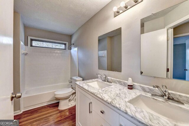 full bathroom featuring a textured ceiling, vanity, toilet, hardwood / wood-style flooring, and tiled shower / bath combo