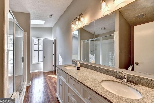 bathroom featuring a shower with shower door, wood-type flooring, a textured ceiling, and vanity