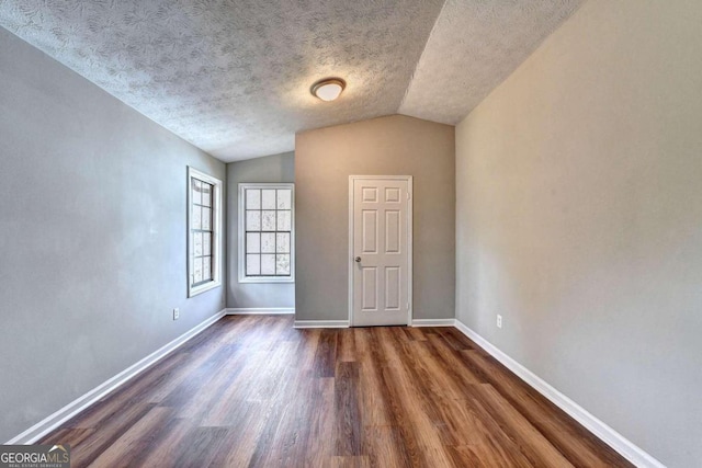 unfurnished room with vaulted ceiling, dark hardwood / wood-style floors, and a textured ceiling