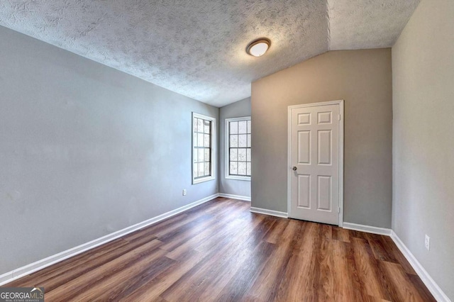 spare room with dark wood-type flooring, a textured ceiling, and lofted ceiling