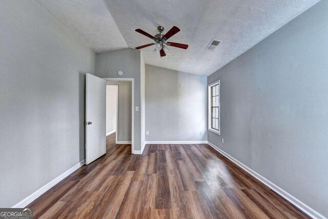 unfurnished bedroom featuring dark wood-type flooring, a textured ceiling, vaulted ceiling, and ceiling fan