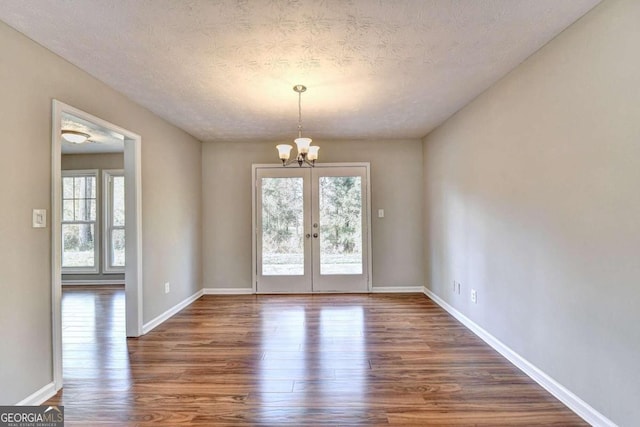 empty room featuring a textured ceiling, plenty of natural light, a chandelier, and dark hardwood / wood-style floors