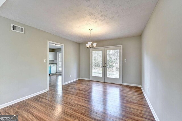 spare room with dark hardwood / wood-style floors, a textured ceiling, a notable chandelier, and french doors