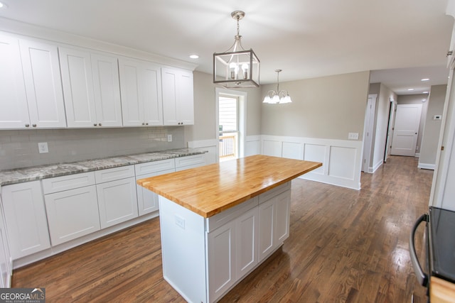 kitchen featuring a center island, light stone countertops, a notable chandelier, white cabinetry, and dark wood-type flooring