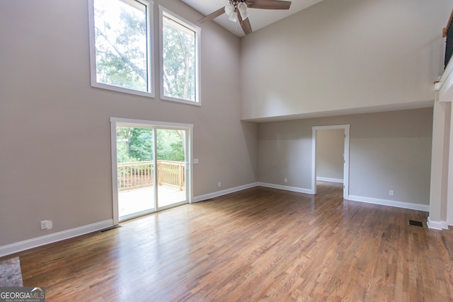 unfurnished living room featuring plenty of natural light, ceiling fan, a towering ceiling, and hardwood / wood-style flooring