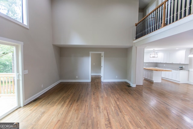 unfurnished living room with hardwood / wood-style flooring, a healthy amount of sunlight, a high ceiling, and a notable chandelier