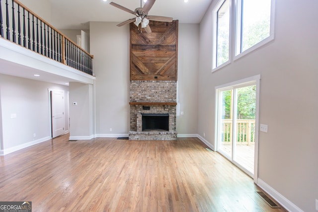 unfurnished living room with a large fireplace, ceiling fan, hardwood / wood-style floors, and a high ceiling