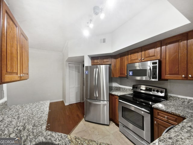 kitchen featuring light stone counters, appliances with stainless steel finishes, brown cabinetry, and visible vents