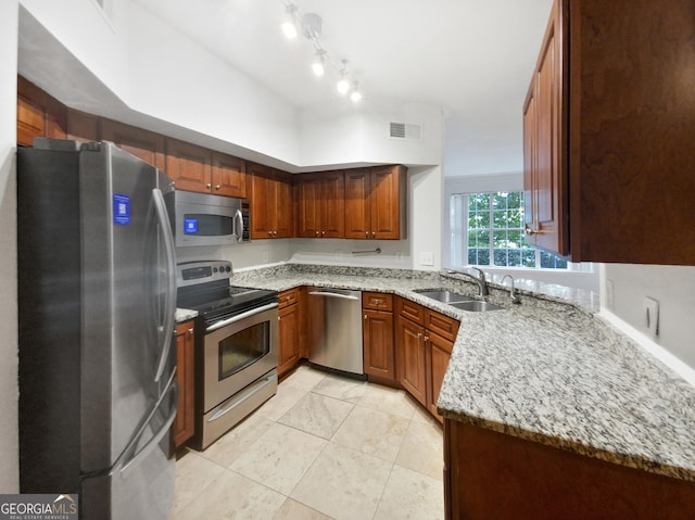 kitchen with light stone counters, visible vents, appliances with stainless steel finishes, brown cabinetry, and a sink