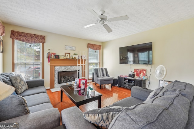 living room featuring ceiling fan, a wealth of natural light, a fireplace, and light hardwood / wood-style floors