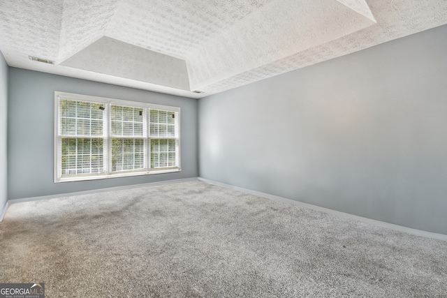 carpeted spare room featuring a textured ceiling and a tray ceiling