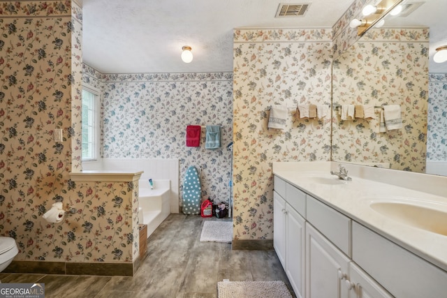 bathroom featuring hardwood / wood-style floors, toilet, a washtub, vanity, and a textured ceiling