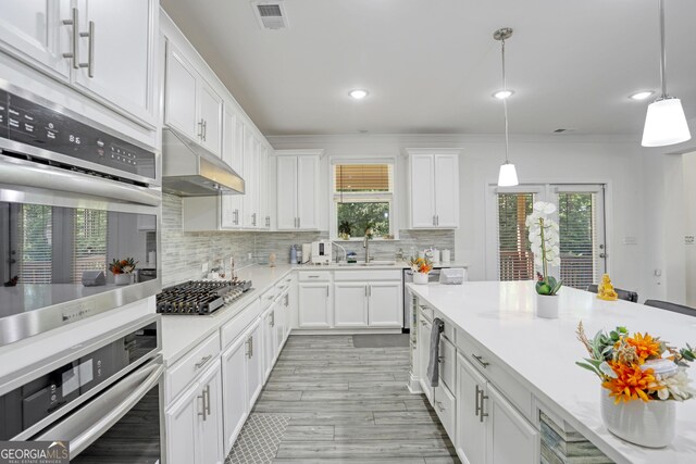 kitchen with white cabinets, decorative light fixtures, backsplash, appliances with stainless steel finishes, and crown molding