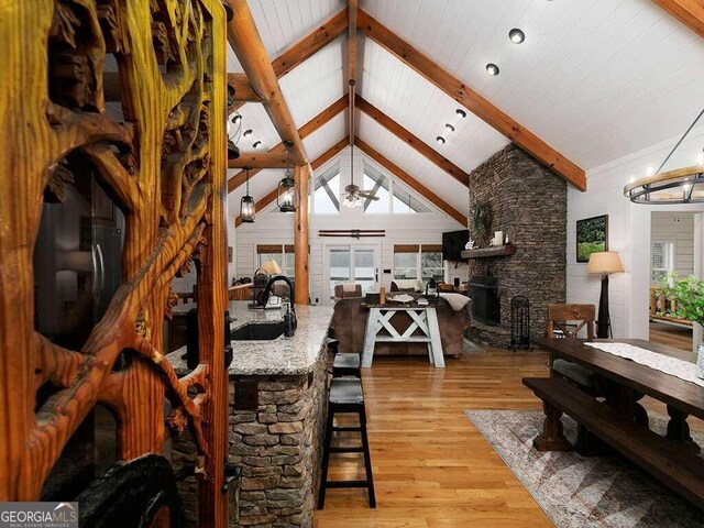 dining area featuring a fireplace, beamed ceiling, a chandelier, sink, and light hardwood / wood-style floors