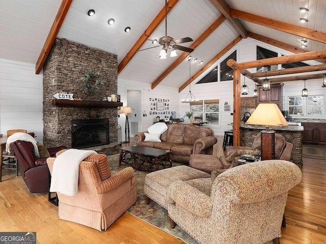 living room featuring wood walls, beamed ceiling, light hardwood / wood-style flooring, a stone fireplace, and ceiling fan