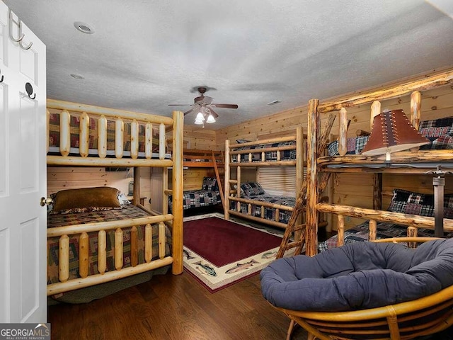 bedroom featuring a textured ceiling, wood-type flooring, wood walls, and ceiling fan