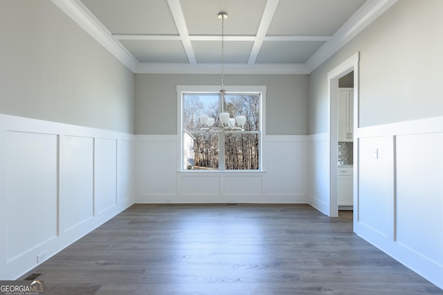 unfurnished dining area with beamed ceiling, coffered ceiling, dark wood-type flooring, and a notable chandelier