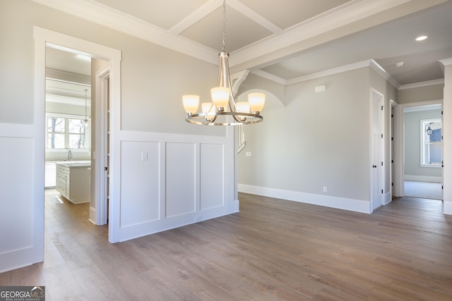 unfurnished dining area with an inviting chandelier, ornamental molding, sink, and light wood-type flooring