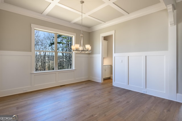 unfurnished dining area featuring beamed ceiling, wood-type flooring, ornamental molding, coffered ceiling, and a notable chandelier