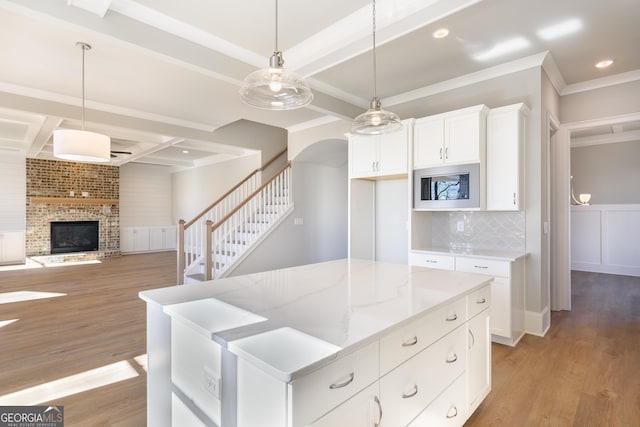 kitchen with light stone counters, decorative light fixtures, stainless steel microwave, light hardwood / wood-style floors, and white cabinets