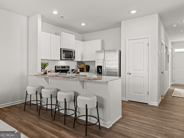 kitchen with dark wood-type flooring, appliances with stainless steel finishes, a kitchen breakfast bar, and white cabinets