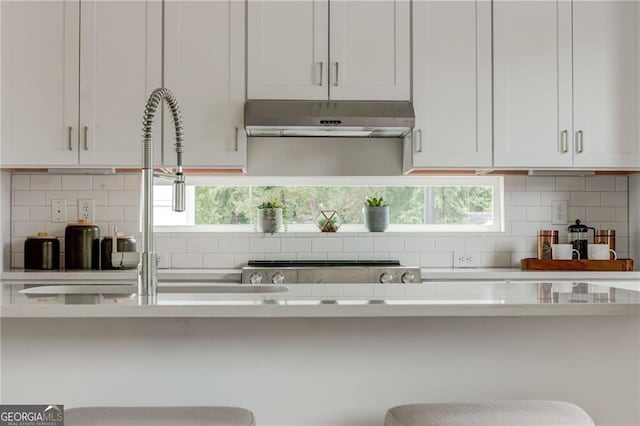 kitchen featuring under cabinet range hood, decorative backsplash, white cabinets, and light countertops