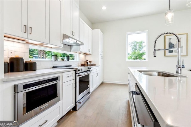 kitchen with plenty of natural light, a sink, under cabinet range hood, appliances with stainless steel finishes, and tasteful backsplash