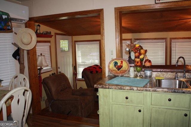 kitchen featuring green cabinets, vaulted ceiling, an AC wall unit, and sink