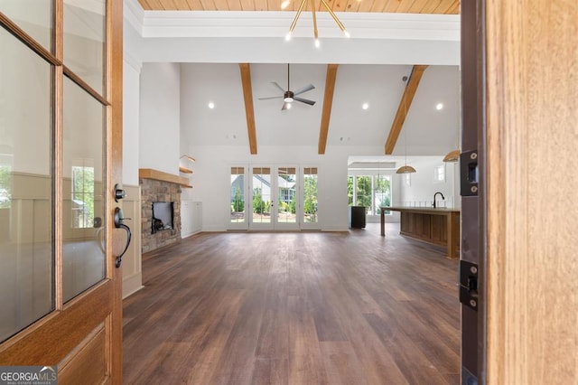 unfurnished living room featuring dark hardwood / wood-style floors, a stone fireplace, beam ceiling, sink, and ceiling fan