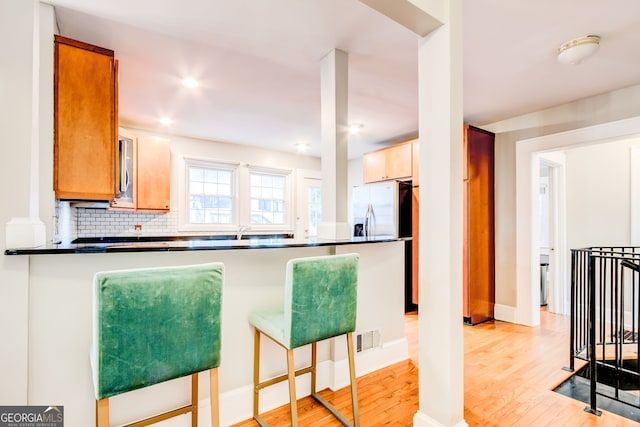 kitchen featuring light hardwood / wood-style floors, backsplash, stainless steel fridge, kitchen peninsula, and a breakfast bar