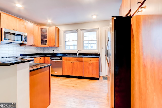 kitchen with decorative backsplash, appliances with stainless steel finishes, sink, and light hardwood / wood-style floors