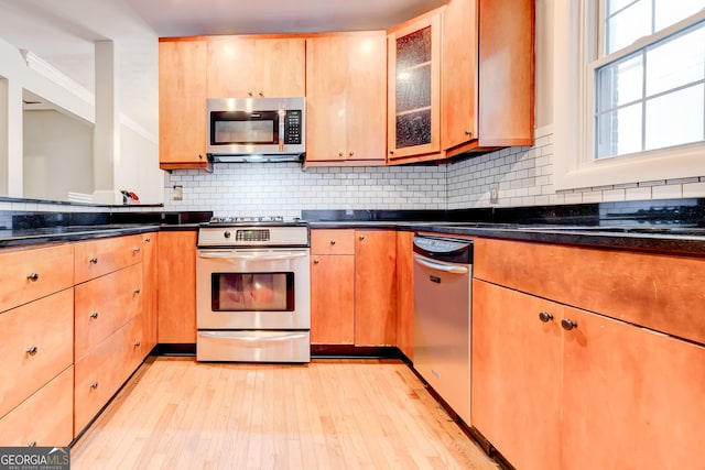 kitchen featuring stainless steel appliances, decorative backsplash, light hardwood / wood-style floors, and dark stone counters