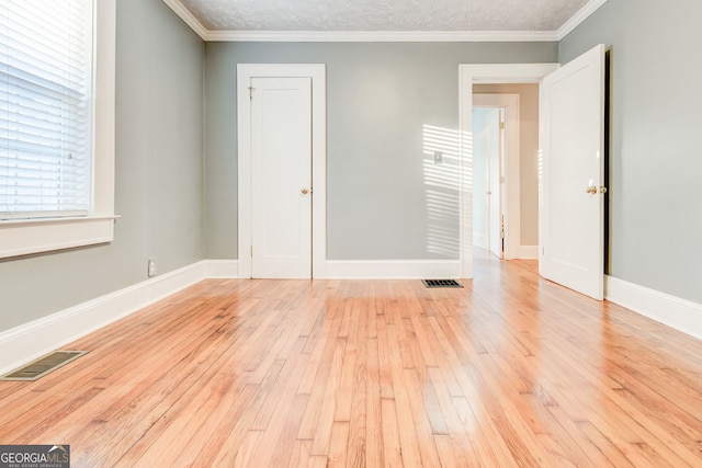 unfurnished room featuring a textured ceiling, crown molding, and light wood-type flooring