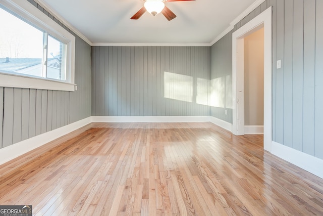 empty room with ceiling fan, ornamental molding, light hardwood / wood-style flooring, and wooden walls