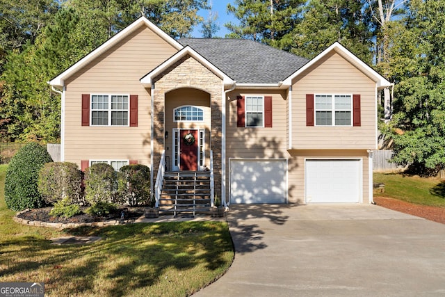 raised ranch featuring driveway, roof with shingles, a front lawn, a garage, and stone siding