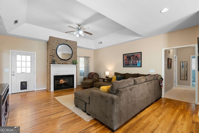 living area featuring a tray ceiling, plenty of natural light, a fireplace, and light wood-style floors