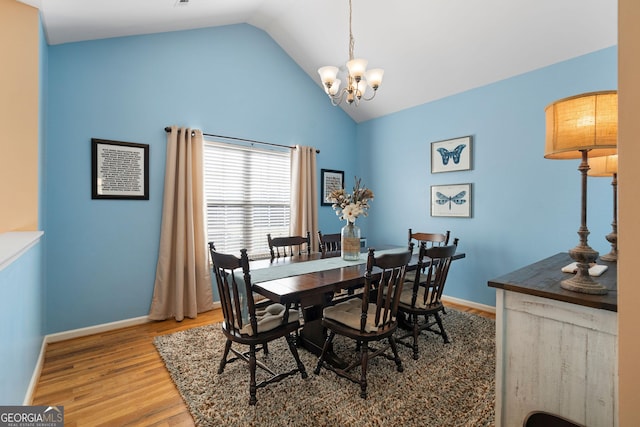 dining room with a notable chandelier, vaulted ceiling, baseboards, and wood finished floors