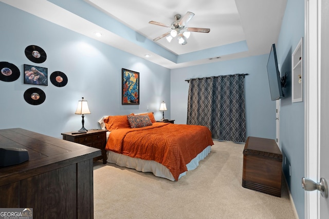 bedroom featuring a tray ceiling, light colored carpet, visible vents, and ceiling fan